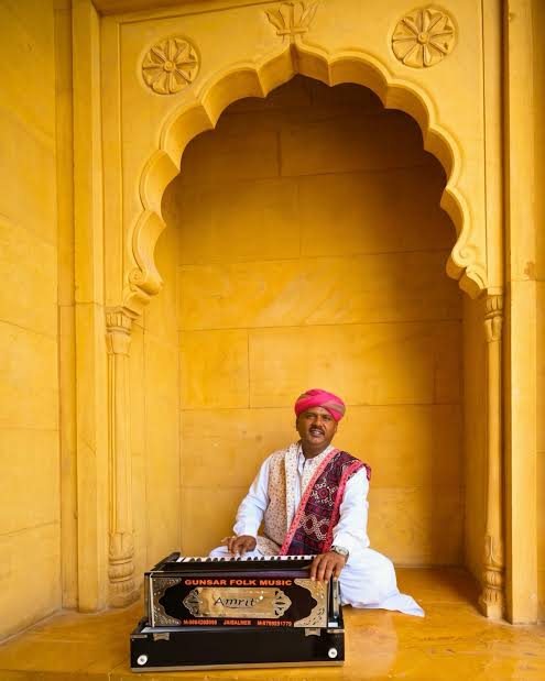 A Manganiyar musician playing harmonium in a sandstone alcove
