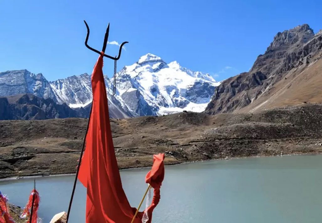 Red pilgrim flags and a trident beside a high-altitude lake